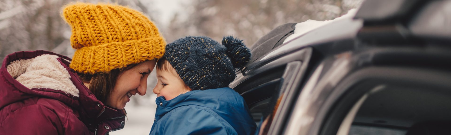 Mujer sonríe a su hijo al lado de un coche. Seguros de coche Allianz.